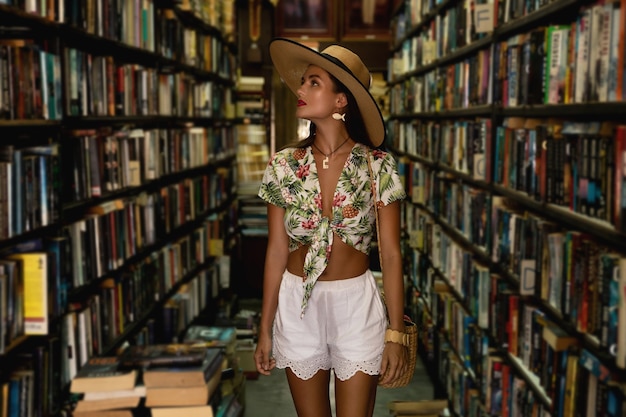 Beautiful girl wearing stylish outfit looking for interesting book in the small vintage bookstore