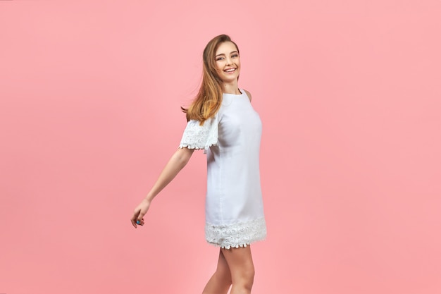 Beautiful girl wearing white dress and posing on pink background.