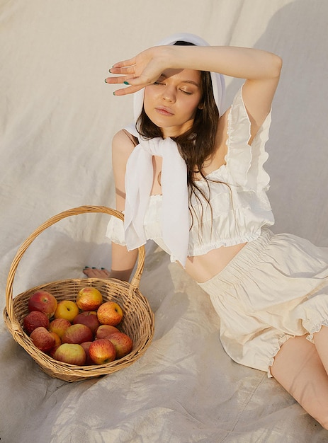 白いブラウスと白いショートパンツと白いヘッドスカーフを着た美しい女の子が ⁇ 布の背景に果物のバスケットを着て ⁇ 夕日ゴールデンアワー