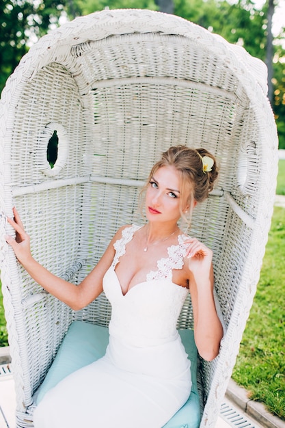 Bella ragazza in una sedia bianca in natura. bionda in un vestito con una scollatura profonda.