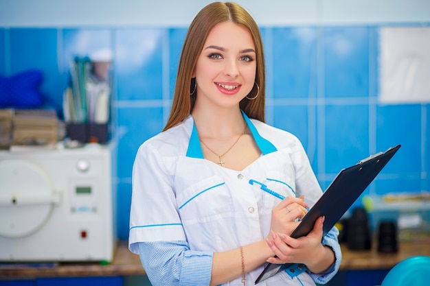 Beautiful girl in a white coat. Image of a woman doctor. Photo of a young woman doctor posing holding clipboard