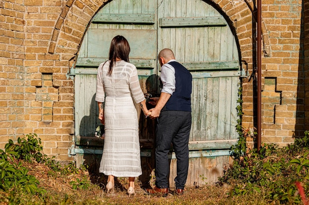 Beautiful girl in a white dress and a guy on the background of a brick wall with an old gate