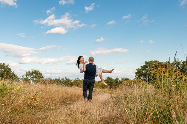 Beautiful girl in a white dress and a guy in a field against a blue sky with clouds