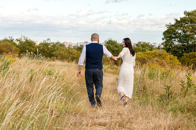 Beautiful girl in a white dress and a guy in a field against a blue sky with clouds