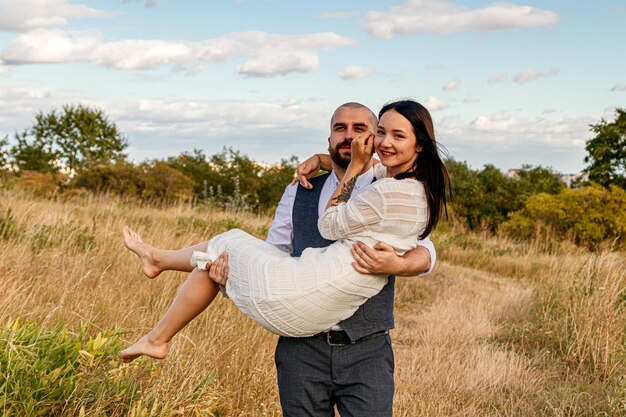 Beautiful girl in a white dress and a guy in a field against a blue sky with clouds