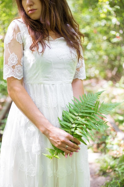 Beautiful girl in white dress holding a fern