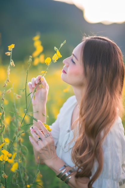 A beautiful girl in a white dress photographed in the middle of a yellow field with flowers at sunset.