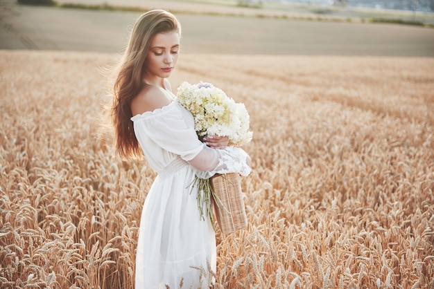 Beautiful girl in white dress running on the autumn field of wheat at sunset time.