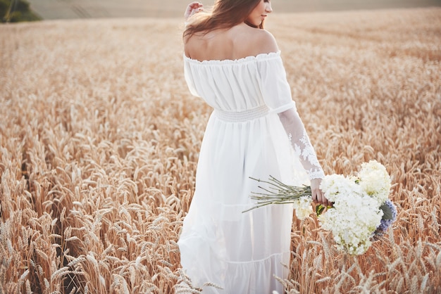 Красивая девушка в белом платье работает на осенние поля пшеницы во время заката.