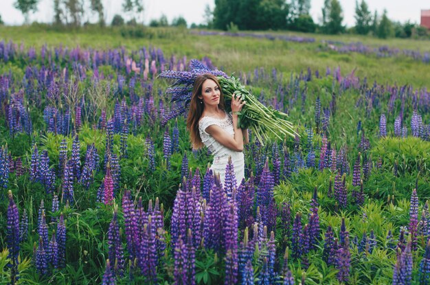 Photo beautiful girl in a white dress standing among the lupines