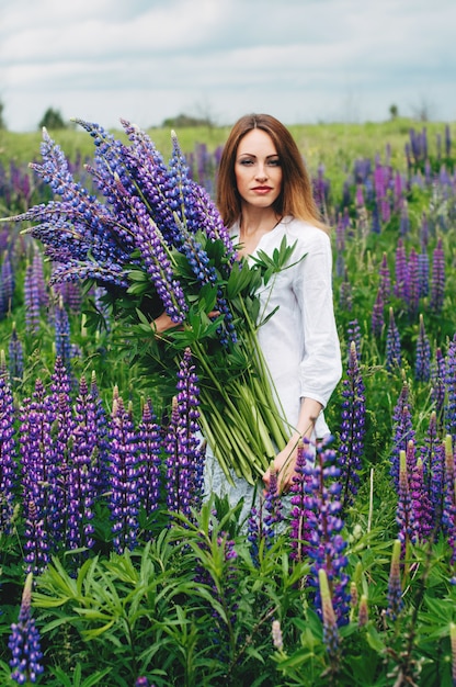 Beautiful girl in a white dress standing among the lupines