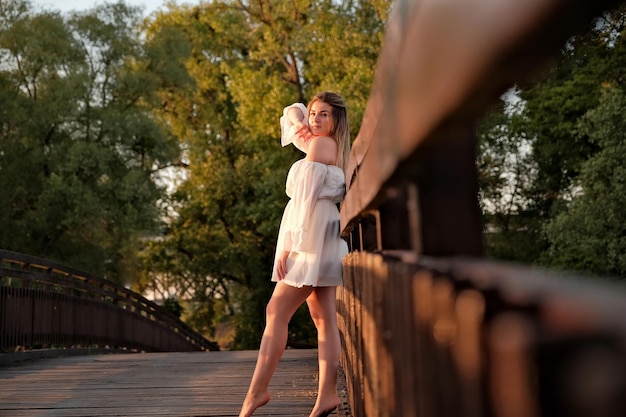 Photo a beautiful girl in a white dress stands on a wooden bridge