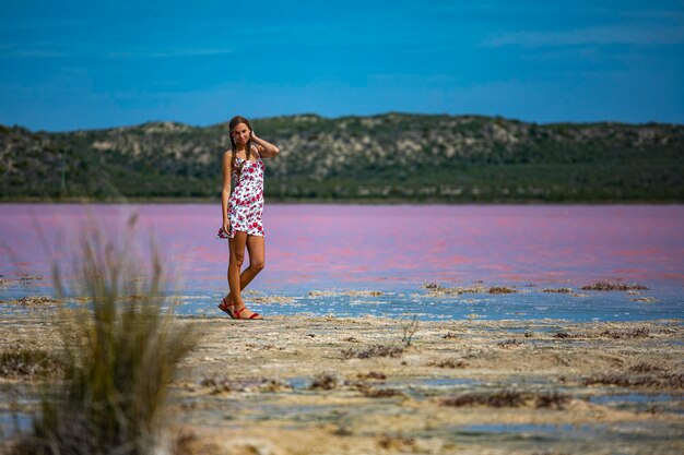 A beautiful girl in a white dress walks along the shore of a pink lake in western australia