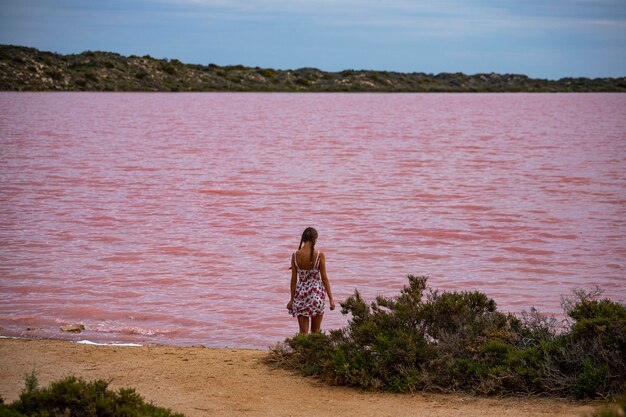 A beautiful girl in a white dress walks along the shore of a pink lake in western australia