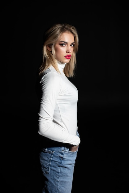 Beautiful girl in white golf and jeans on a black background