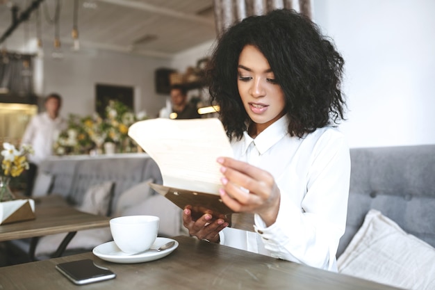 Beautiful girl in white shirt sitting in restaurant with menu in hands