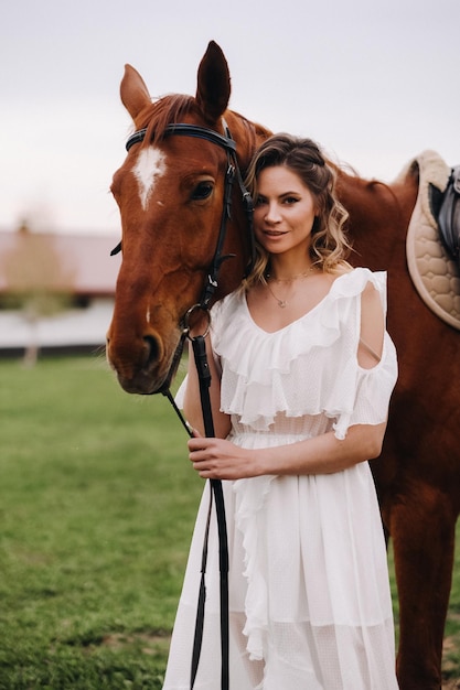 Beautiful girl in a white sundress next to a horse on an old ranch