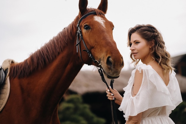 Bella ragazza in un prendisole bianco accanto a un cavallo in un vecchio ranch