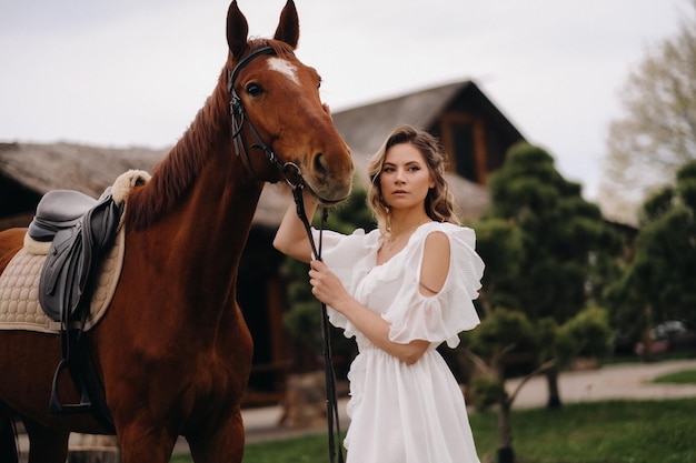 古い牧場の馬の横にある白いサンドレスの美しい少女