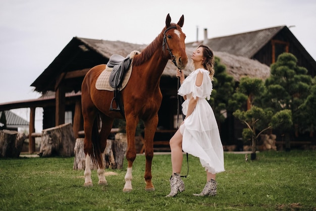 古い牧場の馬の横にある白いサンドレスの美しい少女