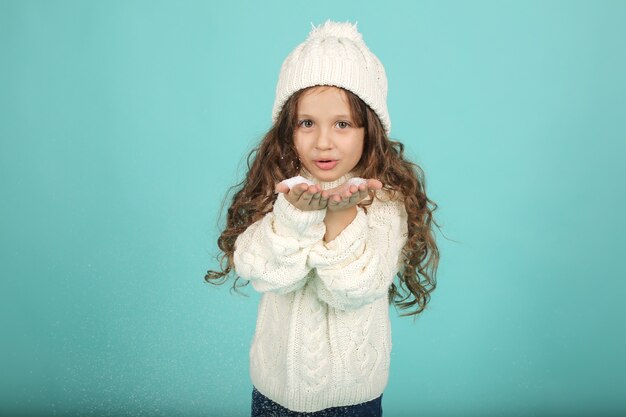 人工雪を吹く白いセーター白い冬の帽子の美しい少女