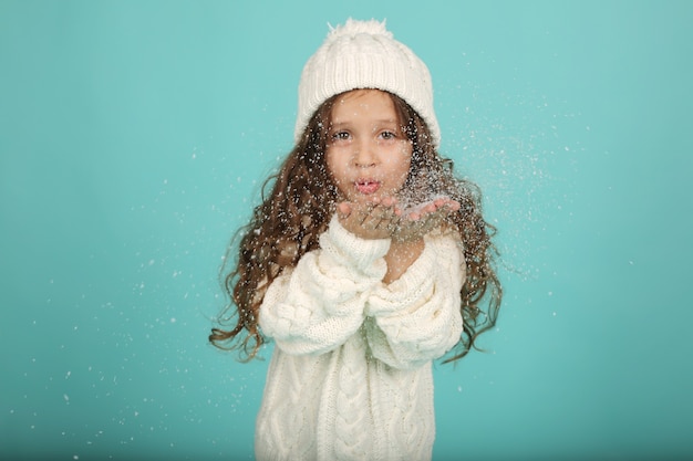 人工雪を吹く白いセーター白い冬の帽子の美しい少女