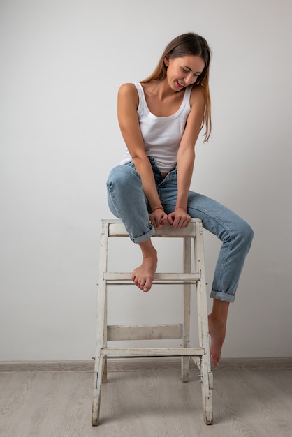 Beautiful girl in a white t-shirt, blue jeans sitting on a chair , smiling and posing