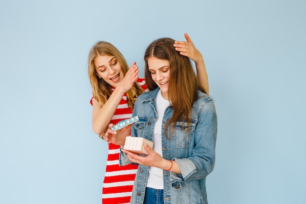 A beautiful girl who makes a gift to her girlfriend and both are happy on a blue  background