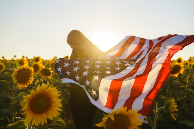 ひまわり畑にアメリカの国旗を持つ美しい少女 7 月 4 日 独立記念日 自由
