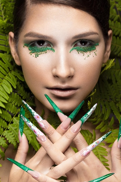 Photo beautiful girl with art makeup fern leaves and long nails manicure design the beauty of the face photos shot in studio