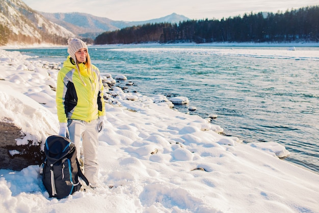 Foto bella ragazza con uno zaino in un fiume di montagna in una giornata invernale