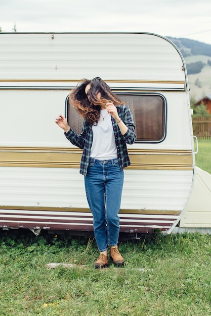 Beautiful girl with backpack traveling Girl standing near trailer traveling in mountains Woman in glasses traveling by car Traveler Girl thumbs up