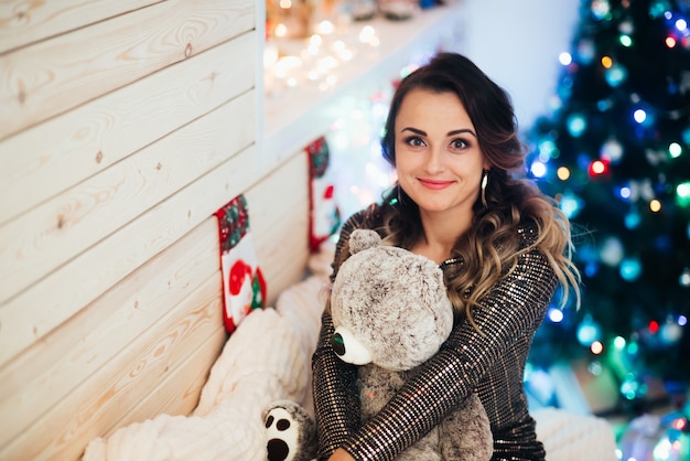 Beautiful girl with a bear in her hands on the background of lights and Christmas tree