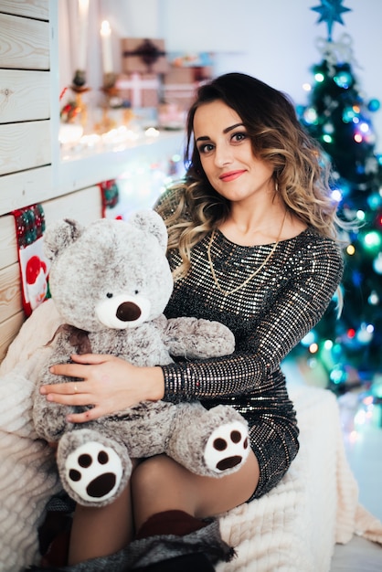 Beautiful girl with a bear in her hands on the background of lights and Christmas tree