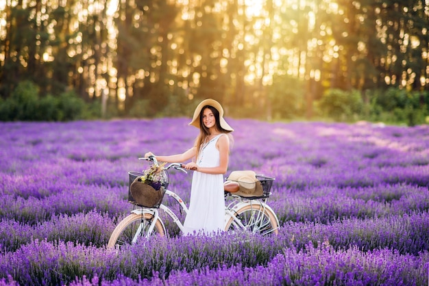 Bella ragazza con una bicicletta in un campo di lavanda. ragazza carina su sfondo viola.