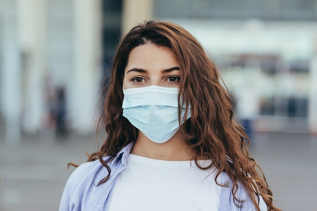 beautiful girl with a big suitcase at the airport wearing a protective mask on her face