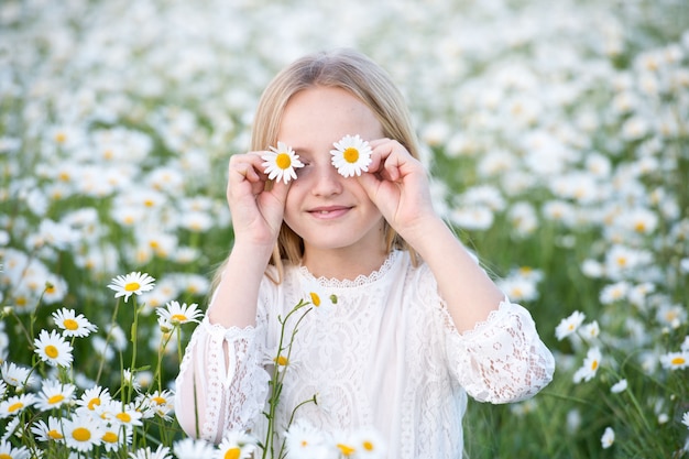 カモミールフィールドでブロンドの髪を持つ美しい少女。夏の草原にカモミールリースで美しい少女。