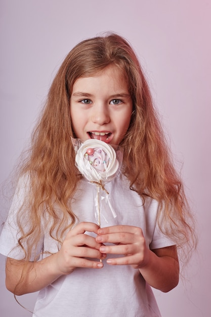 Beautiful girl with blond hair eats a Lollipop, round caramel on stick in hands of cheerful smiling girl