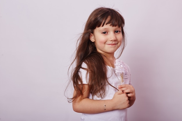 Bella ragazza con capelli biondi mangia un lecca-lecca, caramello rotondo sul bastone nelle mani della ragazza sorridente allegra.