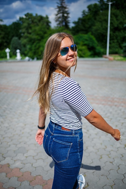 A beautiful girl with blond long hair of European appearance. Dressed in jeans and a T-shirt. Walk on a sunny day