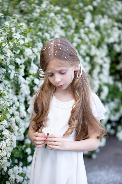 beautiful girl with blond long hair in a white delicate silk dress stands in the park