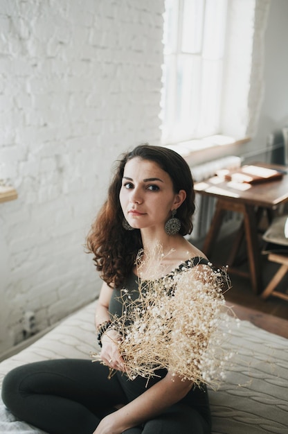 A beautiful girl with a bouquet of flowers is sitting on the bed