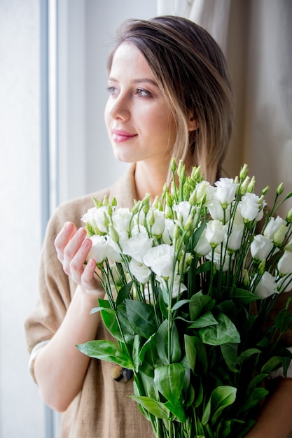 Bella ragazza con un mazzo di rose bianche in piedi vicino a una finestra a casa