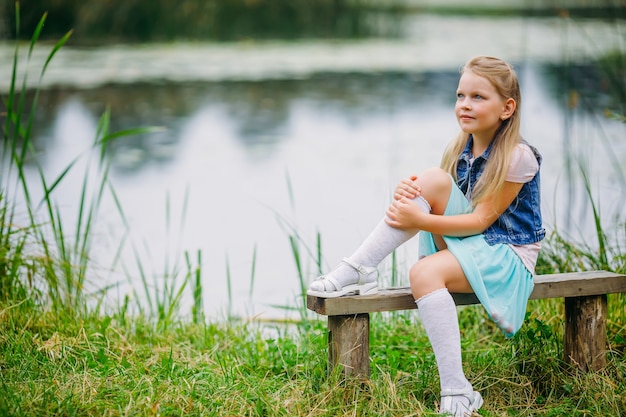 A beautiful girl with bright blue eyes sits in the park on a bench and looks into the distance