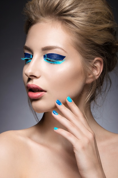 Beautiful girl with bright creative fashion makeup and blue nail polish.