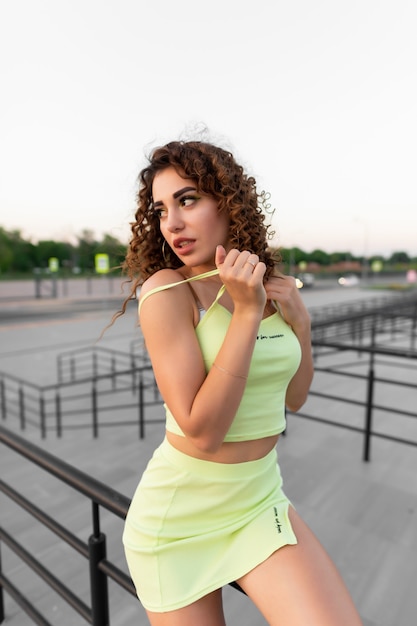 Beautiful girl with curls in a green skirt and top posing against the background of the city
