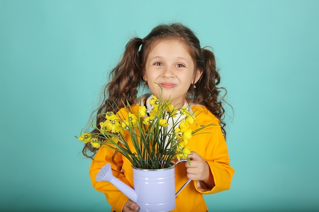 a beautiful girl with curly hair in a yellow jacket holds a watering can with flowers