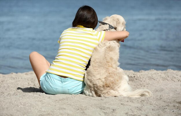 Beautiful girl with cute retriever on river shore