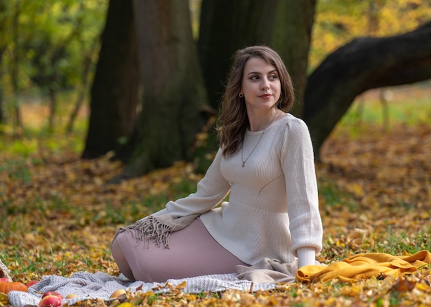 A beautiful girl with dark hair and big eyes sits on the grass autumn walk in the park