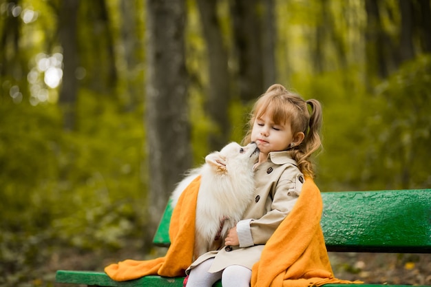 Beautiful girl with a dog is sitting on a bench in the park